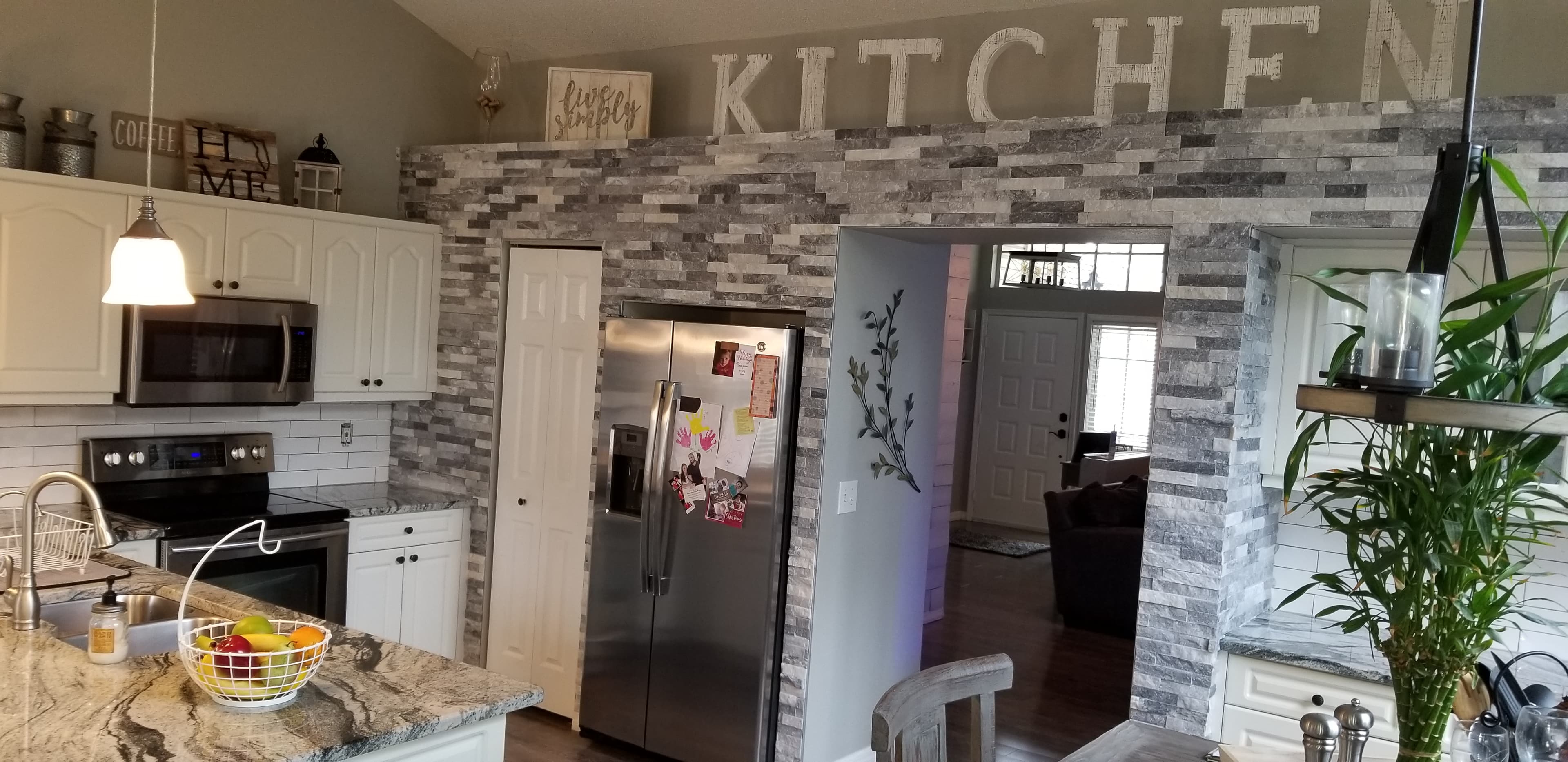 Remodeled farmhouse style kitchen with stacked stone accent wall, white cabinets, and granite countertops